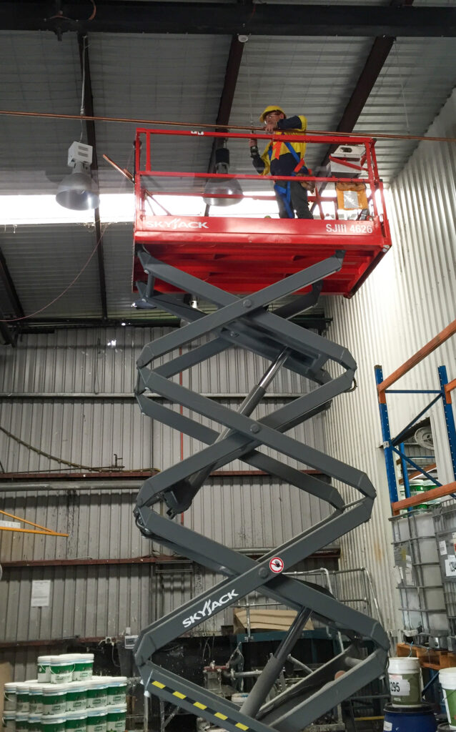 workman on scissor life installing pipes